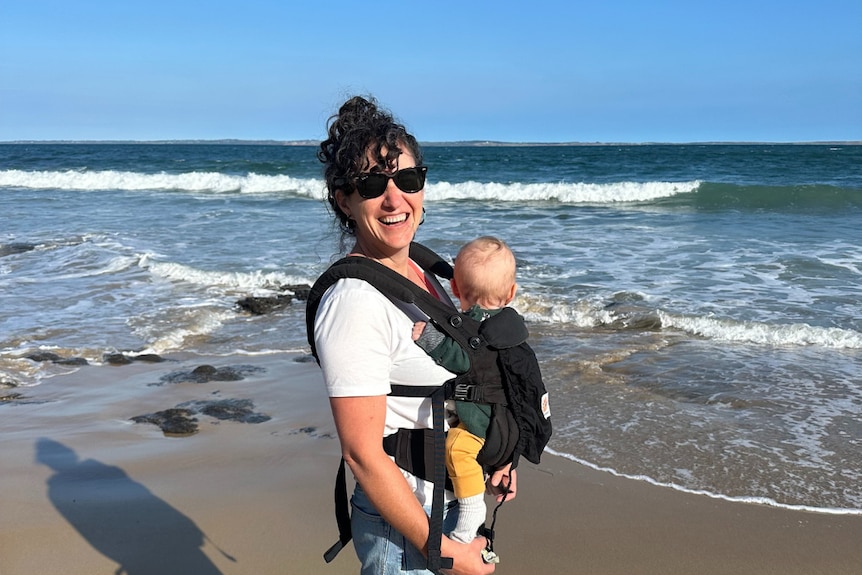 A woman smiling while she holds a baby at the beach