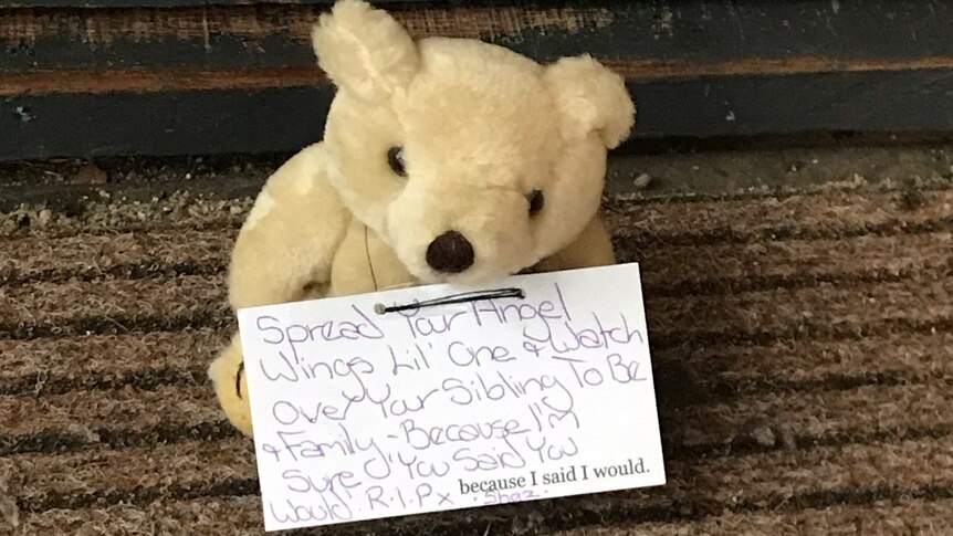 A small teddy bear holds a card with a written message.