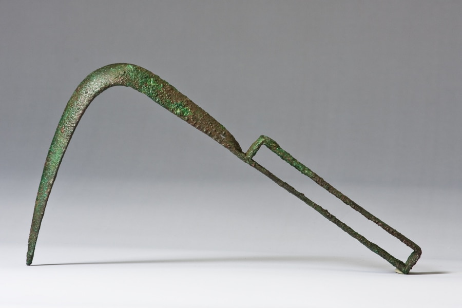 A green patinaed bronze object with a curved blunt blade.