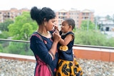 A mother holds her young daughter on a balcony. 