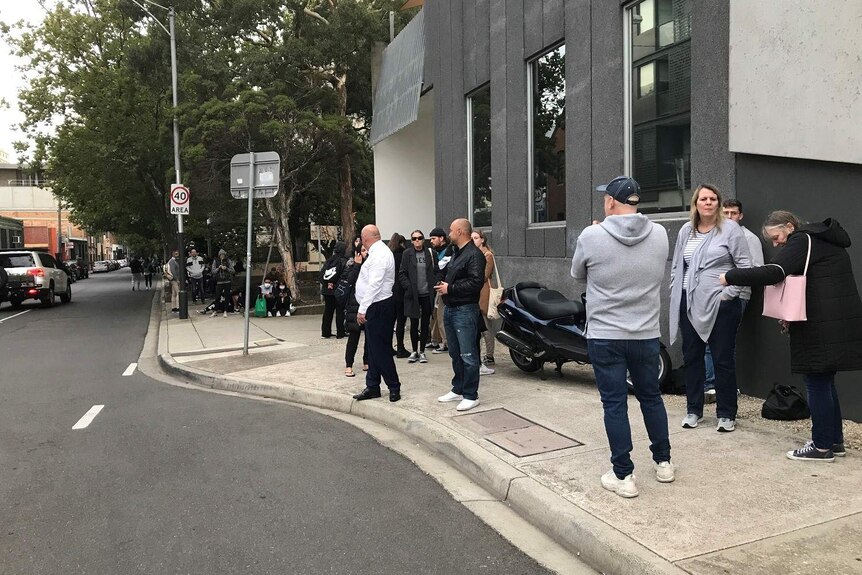 About a dozen people stand outside a grey building in Melbourne.