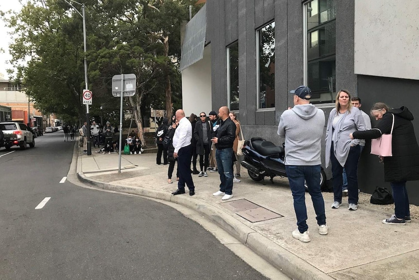 About a dozen people stand outside a grey building in Melbourne.