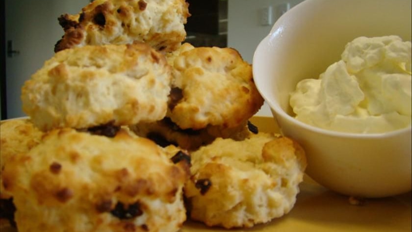 A pile of scones with a bowl of cream beside them.