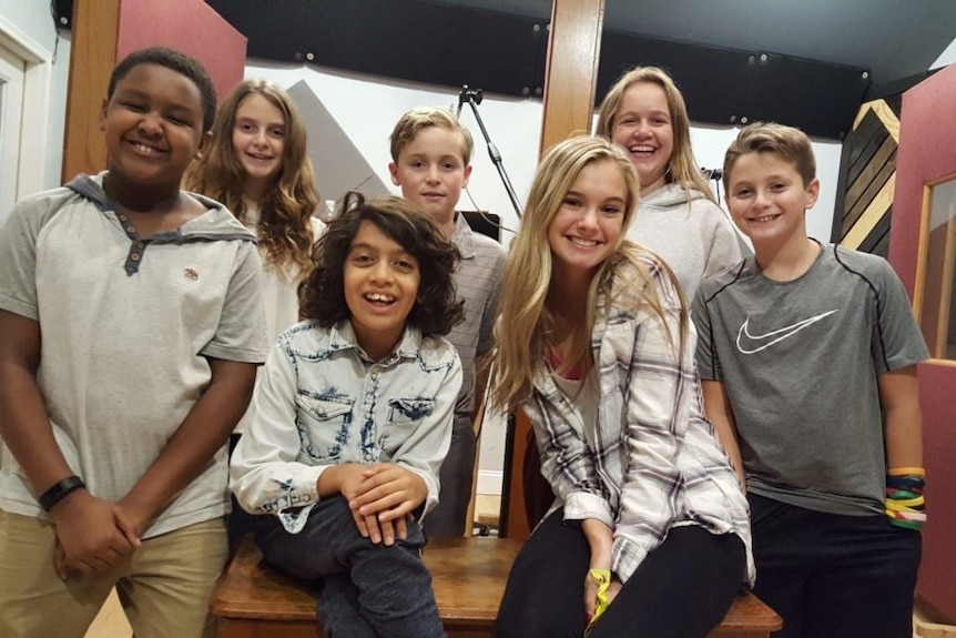 A group of seven children with big smiles on their faces post for a photo in a radio studio.