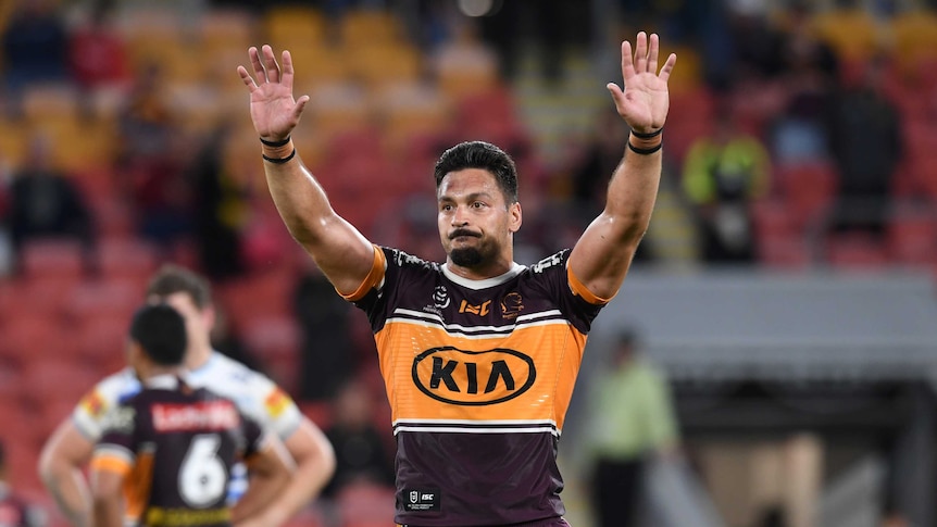 Alex Glenn holds his hands up to the crowd wearing a maroon and yellow rugby jersey