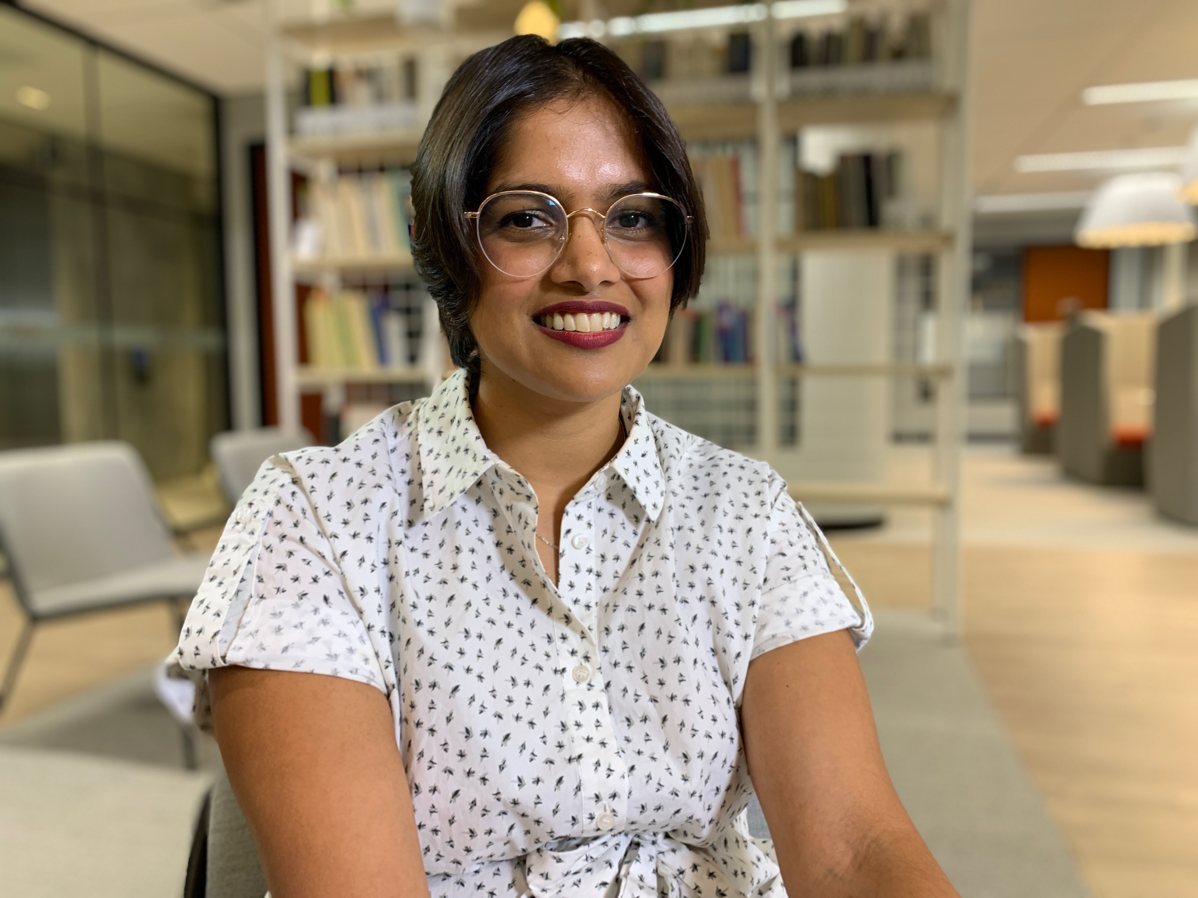 Gabriela D'Souza is senior economist at CEDA, sitting on a chair in front of books.