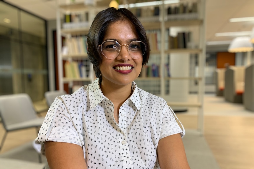 Gabriela D'Souza is senior economist at CEDA, sitting on a chair in front of books.