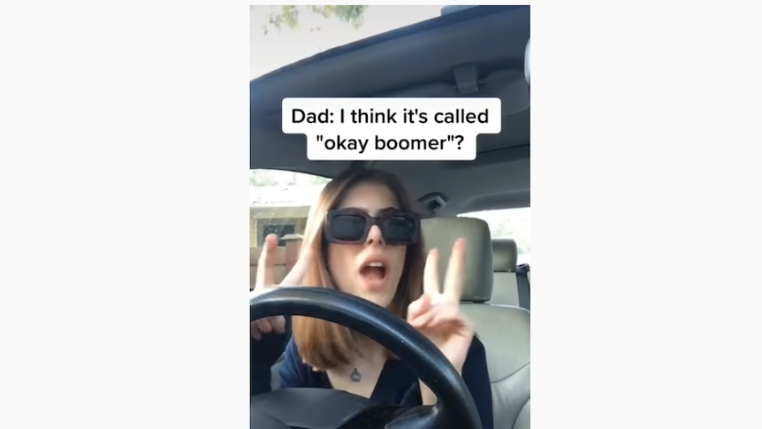 A woman does air quotes while sitting in the driver's seat of a car, with the subtitles "Dad: I think it's called 'ok boomer'"