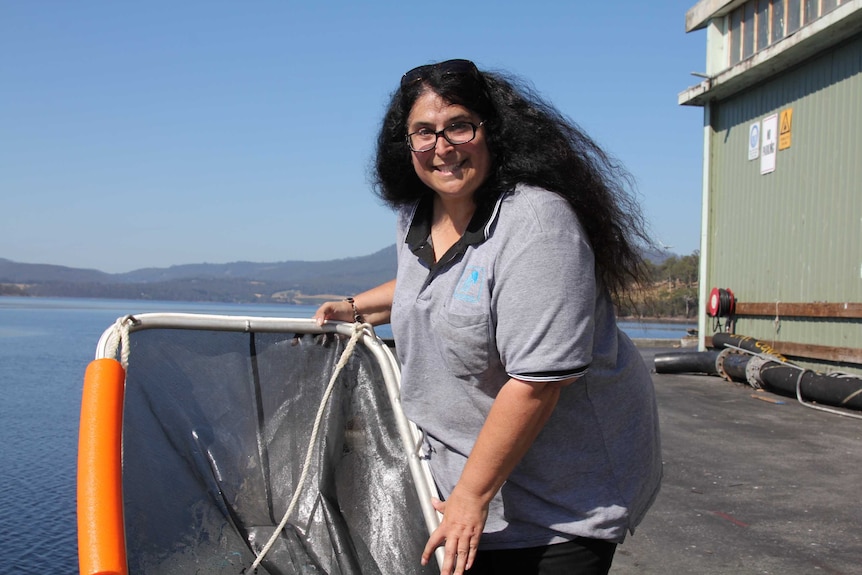 a woman with long dark holds a net on a wharf