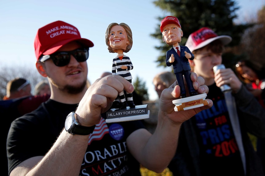 Man holds bobble-head dolls of Clinton and Trump