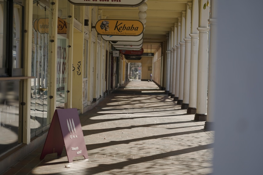 La strada è vuota e ombreggiata, le attività commerciali sono chiuse.