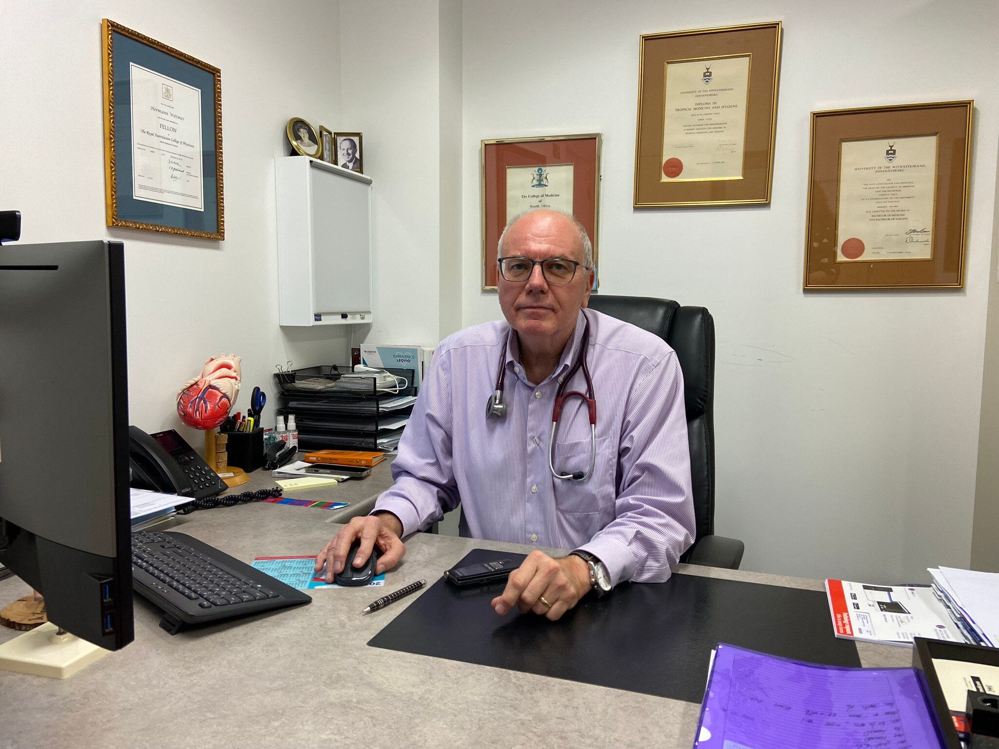 A wide shot of a doctors office with a man sitting in the middle of frame at his desk
