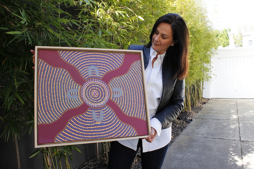 A woman looks at an indigenous dot artwork with four wavy lines coming into a circle