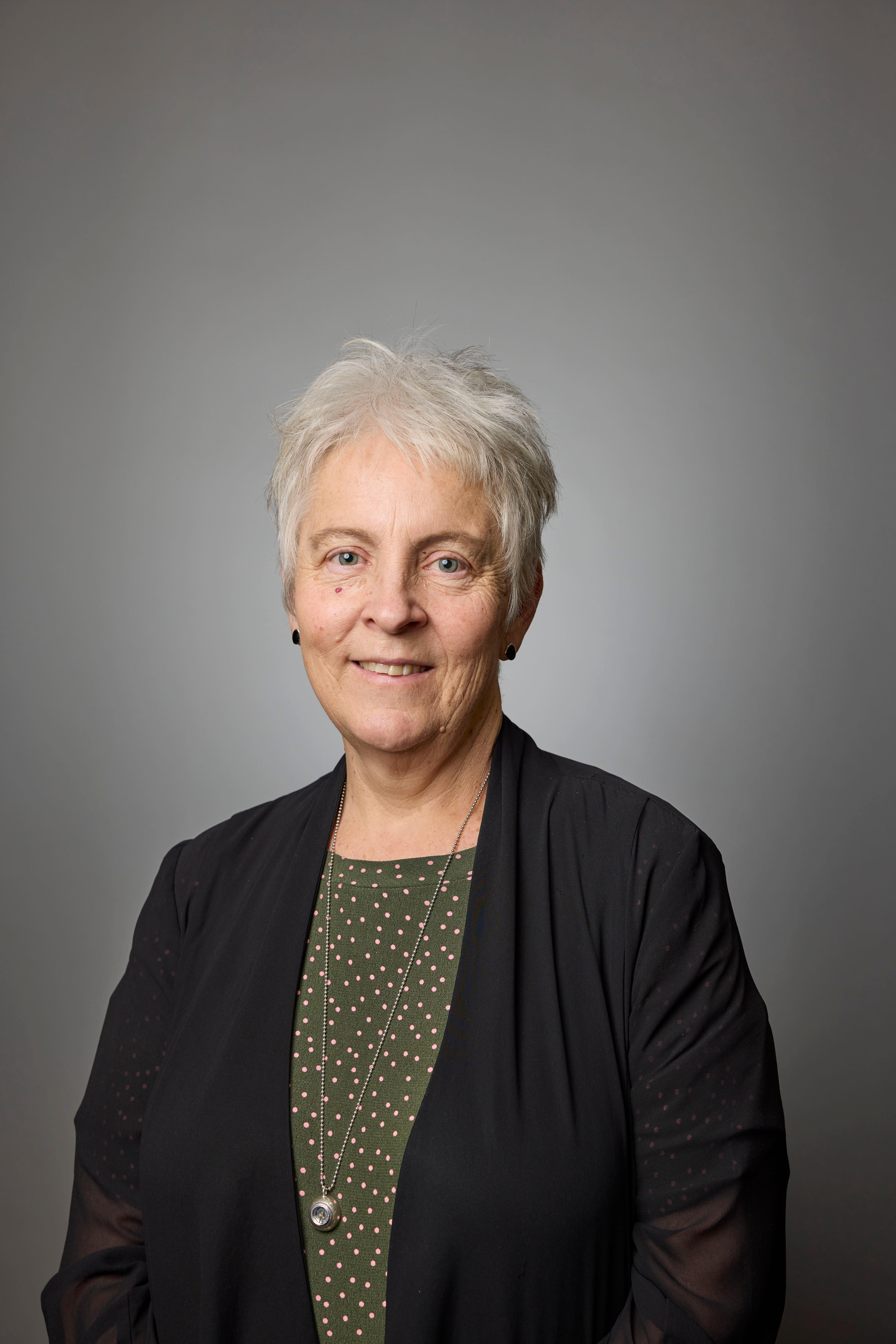 Mulher de terno com cabelos grisalhos sorri na frente de um fundo cinza