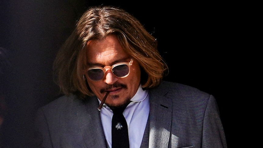 Johnny Depp walks out of a courthouse in a grey suit with his head down.