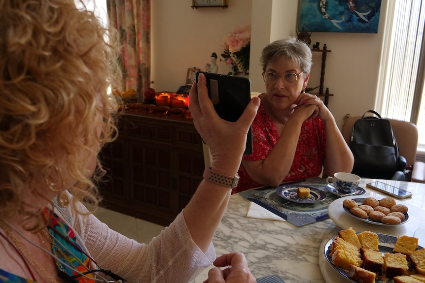 A woman holds up a phone to another lady at morning tea.