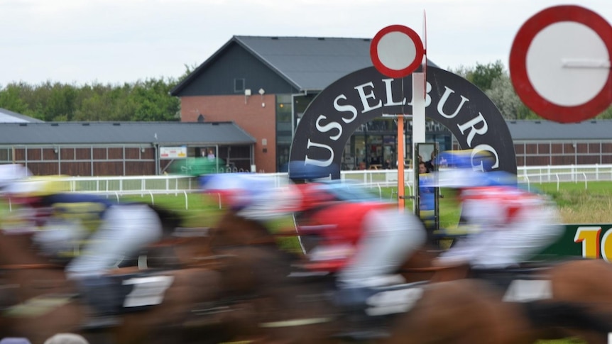 Horses run past a finishing post with Musselburgh written on it in a blur