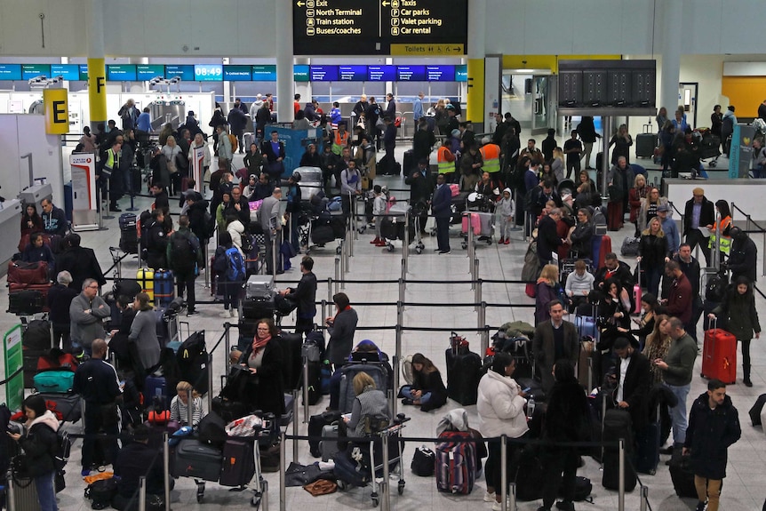 Dozens of people dressed in thick winter clothing stand around inside an airport terminal.