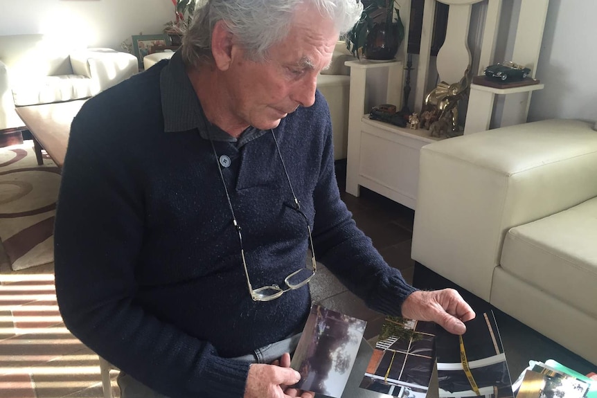 Bernie King in his home looking at photos of his house during asbestos cleaning.