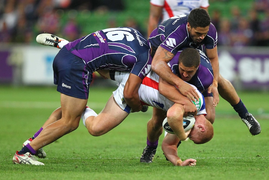 Alex McKinnon of the Newcastle Knights is tackled by the Melbourne Storm on March 24, 2014.