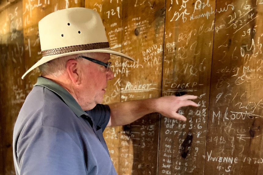 A man wearing a hat looks at writing on a timber wall