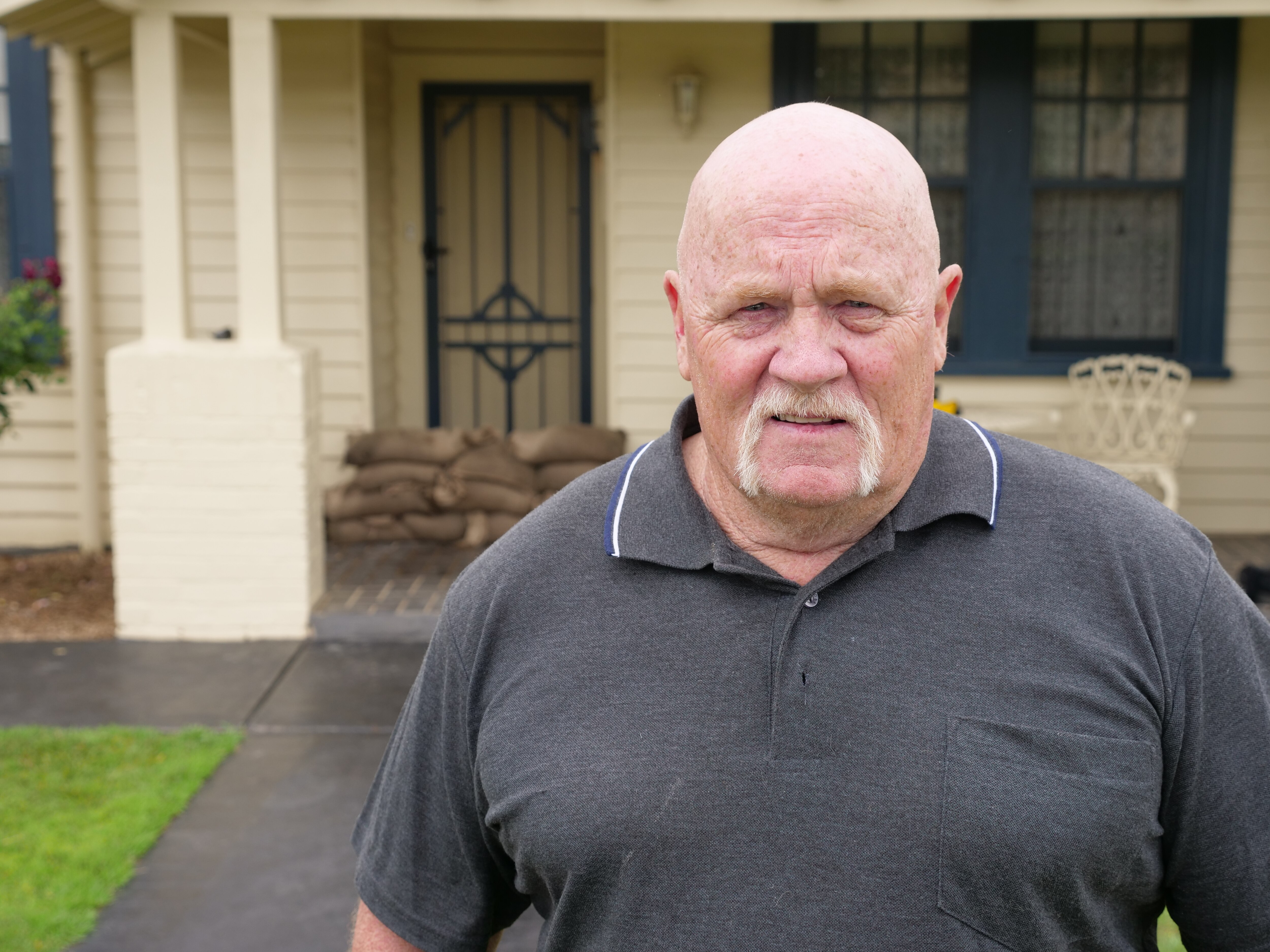 A bald man standing in front of a house with sandbags at the door