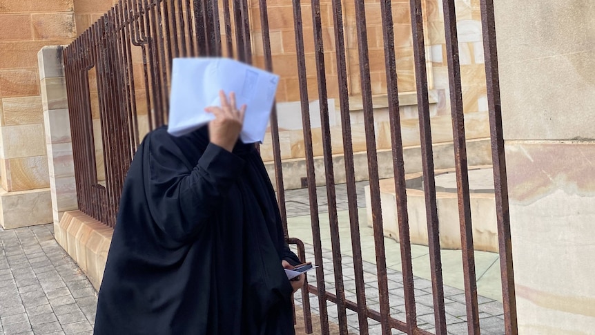 A woman in black clothing covers her face with white envelope