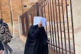 A woman in black clothing covers her face with white envelope