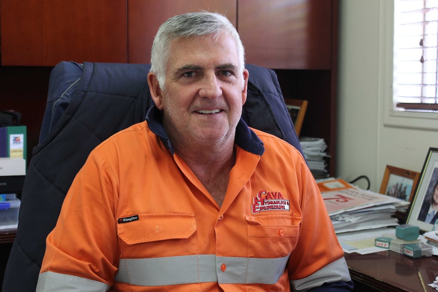 A man in a high visibility shirt smiles as he sits in an office.