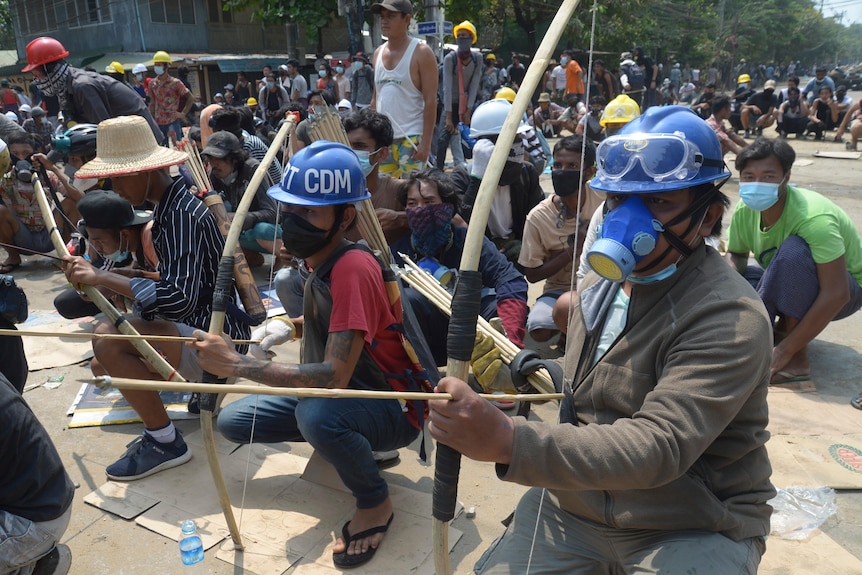 Anti-coup protesters use makeshift bow and arrows while wearing face masks. 