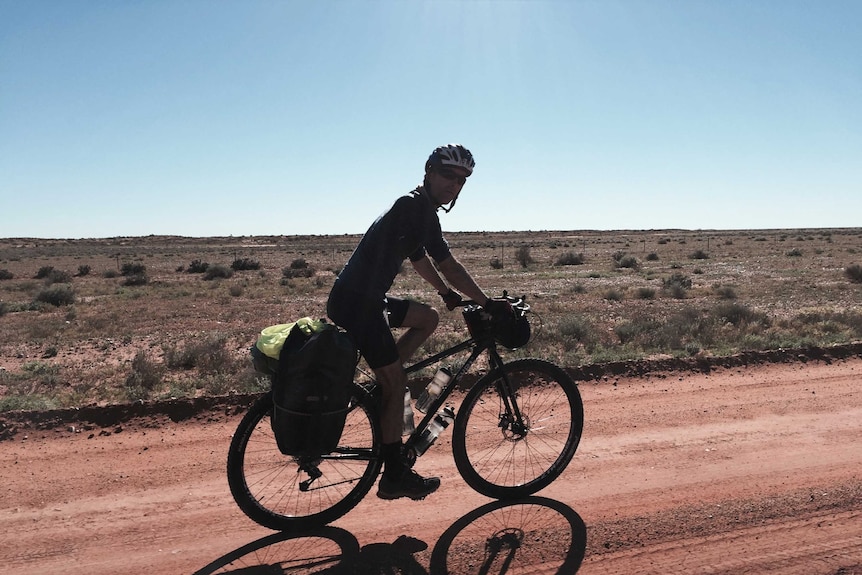 One cyclist on a dirt track with vast outback plains in background