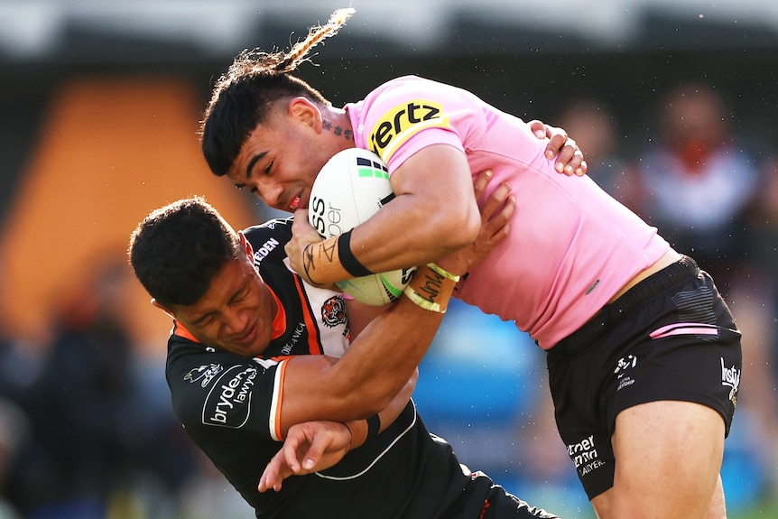 A Penrith Panthers NRL player is tackled by a Wests Tigers opponent.
