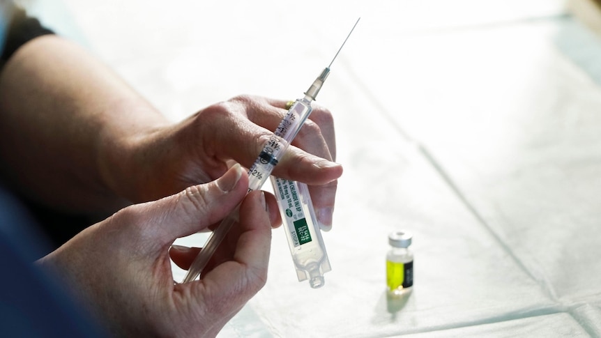 Nurse holding vaccination needle with Pfizer vial nearby.