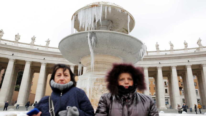 People stand in front of a frozen fountain on a cold winter day in Saint Peter's square at the Vatican.