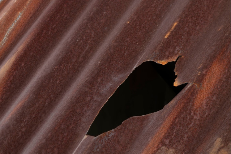 An 18cm hole is visible in a rusted corrugated tin section of roofing