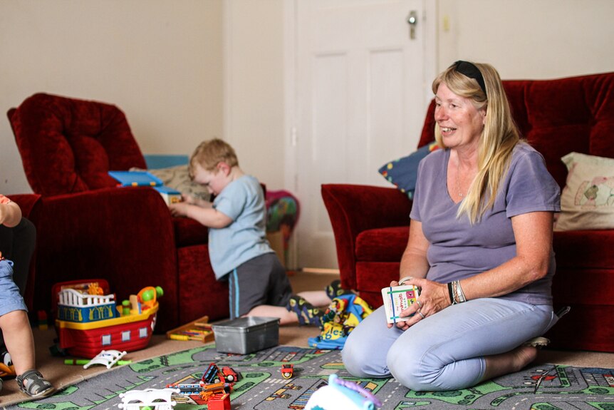 Family day care provider Alvina Brooks in the lounge room with one child in the background playing with a toy.