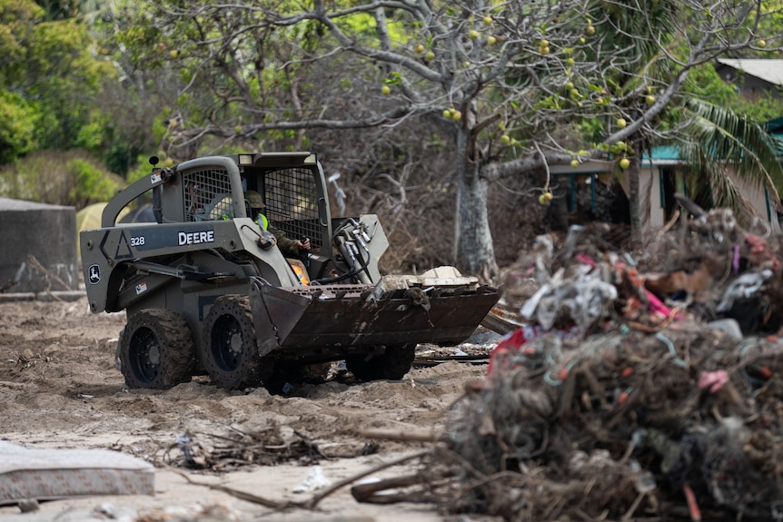 A bobcat carries debris among wreckage on an island in Tonga.