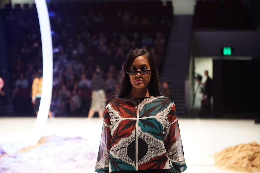 A woman wearing sunglasses poses on a fashion runway