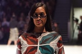 A woman wearing sunglasses poses on a fashion runway.