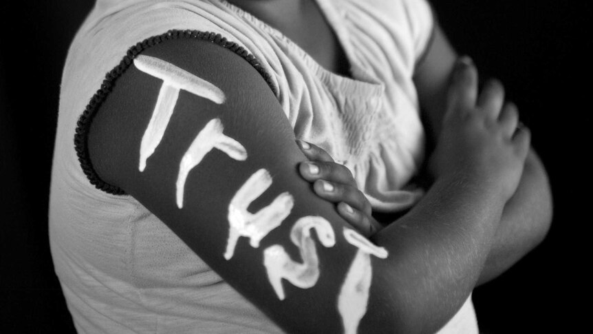 A black and white photo of a child with the word trust painted on one arm