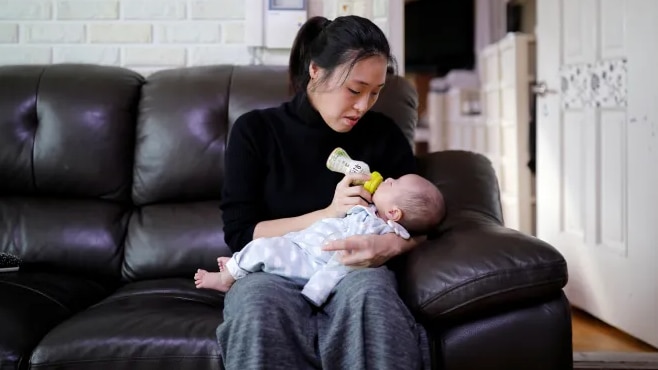 A woman wearing a black top holding a baby while sitting on a couch