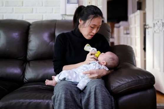 A woman wearing a black top holding a baby while sitting on a couch