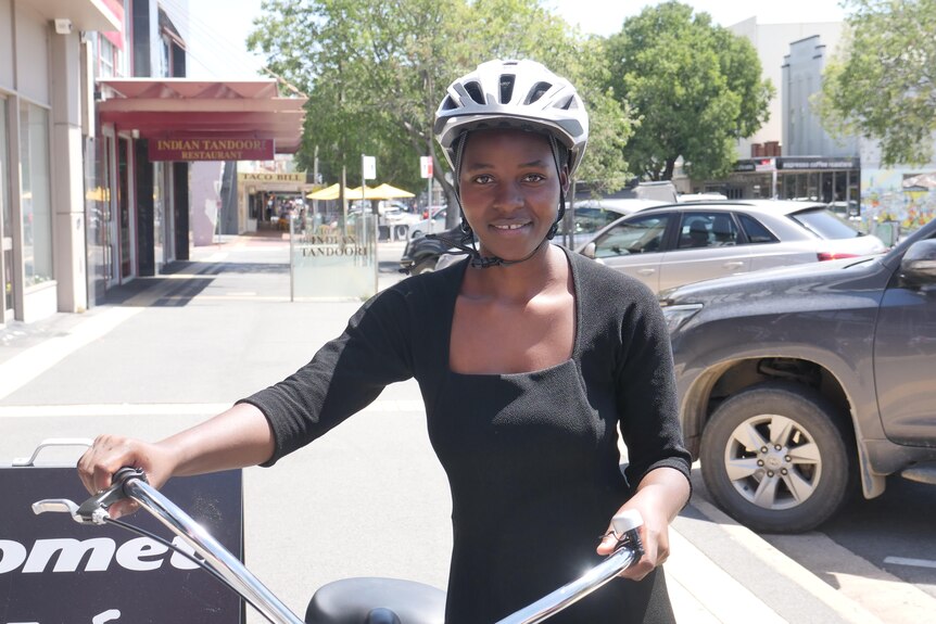 A woman standing beside a bike on a street, holding the handles and wearing a helmet