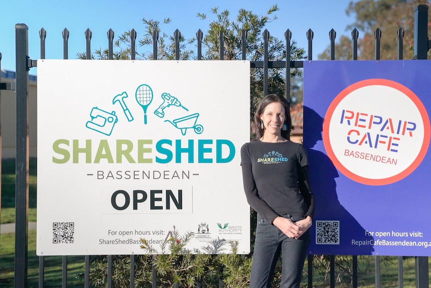 A woman in black cloths standing in front of a sign for the Bassendean share shed. 