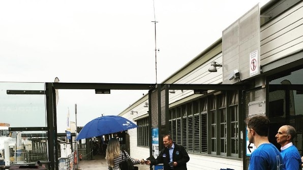 Tony Abbott hands a flyer to a woman near a ferry stop