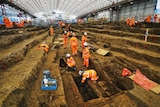 Under a huge marquee dozens of archaeologists are working to exhume skeletons.