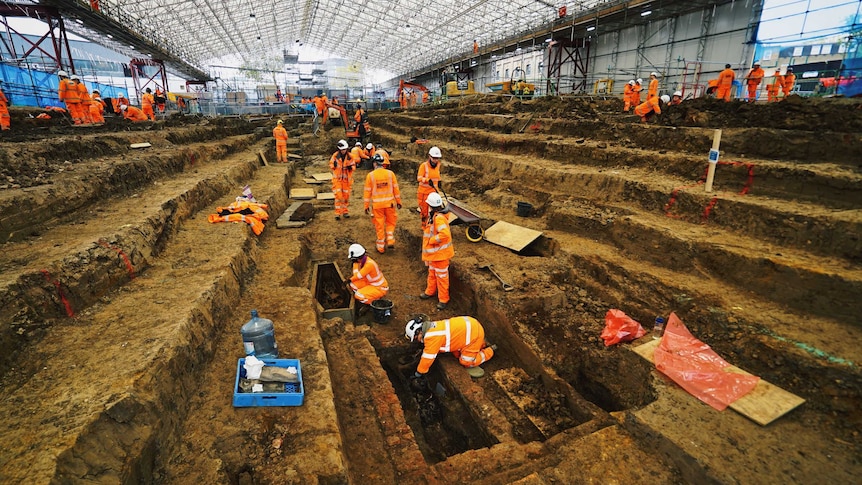 Under a huge marquee dozens of archaeologists are working to exhume skeletons.