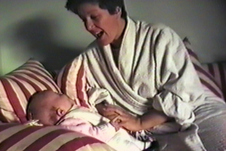 a woman wearing a bathrobe sitting on a sofa with a newborn baby