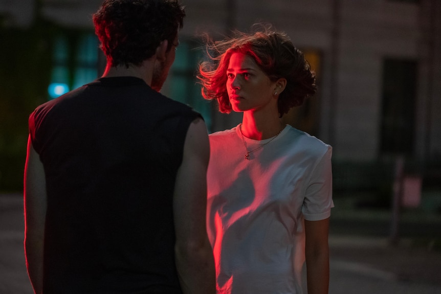 A film still of Zendaya facing Josh O'Connor at night. She is lit by red light, and her hair is whipping in the wind.