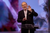 a man standing behind a lectern holding up his hand